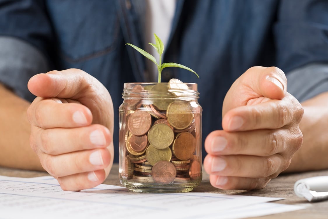 Mains qui protègent un bocal en verre rempli de pièces